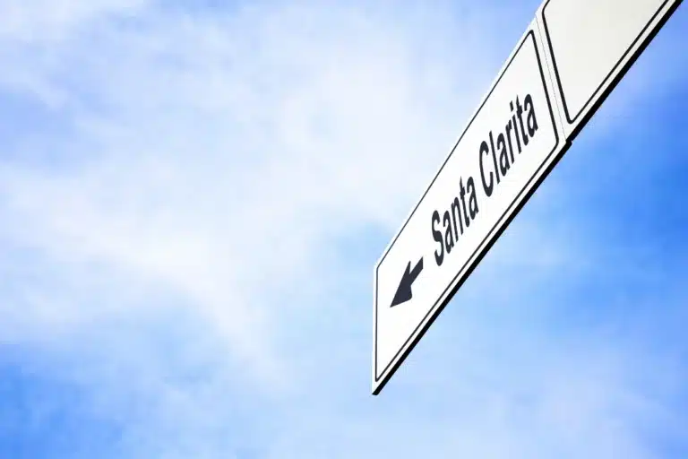 A directional road sign pointing left with the text 'Santa Clarita' against a clear blue sky.