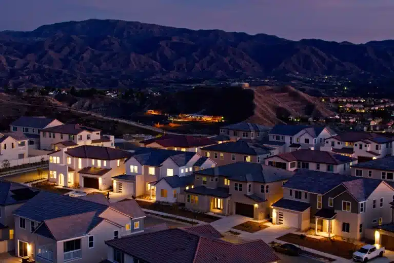 A scenic night view of a residential neighborhood in Santa Clarita, California, with warmly lit houses and surrounding hills in the background.