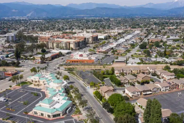 Aerial view of West Covina’s commercial and residential neighborhoods, showcasing accessible shopping centers, housing, and mountain views in the background.