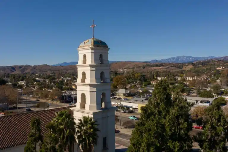 Historic mission-style bell tower overlooking the city of Pomona, California, with mountains in the background under a clear blue sky.