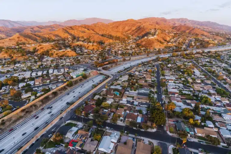 Aerial view of Burbank neighborhoods and freeway surrounded by golden hills at sunset.