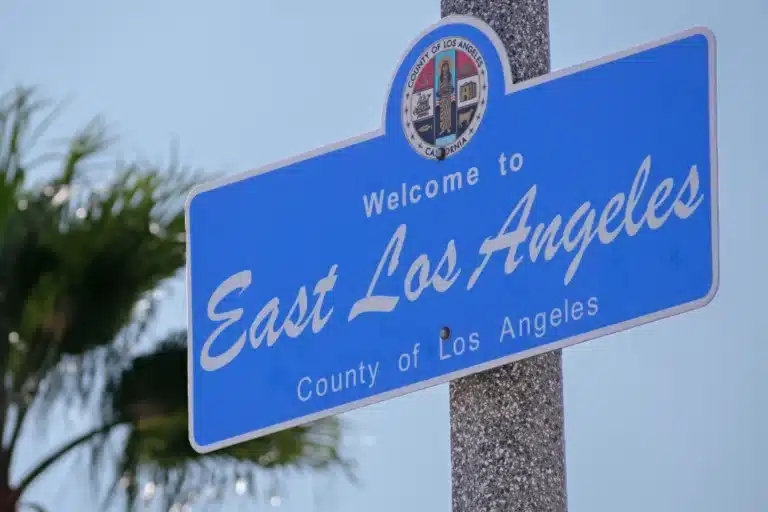 Welcome to East Los Angeles blue road sign with city emblem and clear sky background.